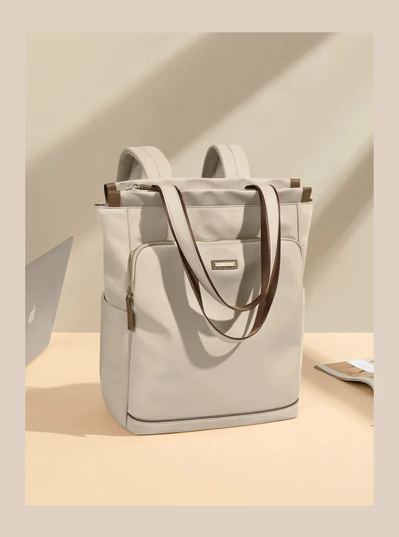 Light gray backpack with brown straps on a beige surface