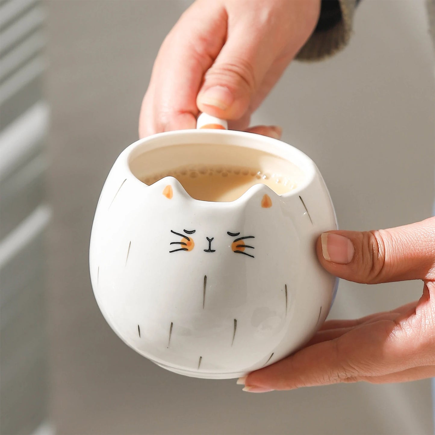 Person holding a white ceramic mug with cat face design filled with coffee.