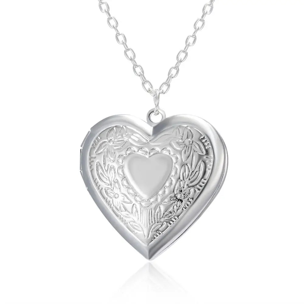 Silver heart-shaped locket with intricate designs on a white background