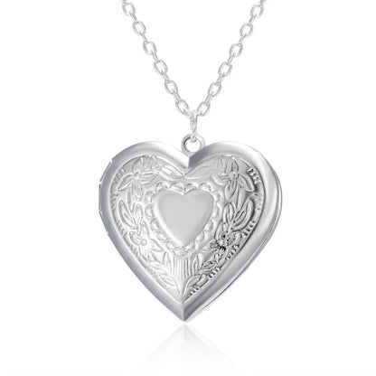 Silver heart-shaped locket with intricate designs on a white background