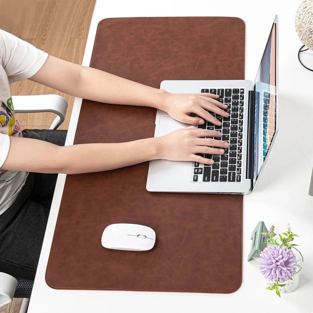 Person using a laptop on a brown desk pad with a white mouse.