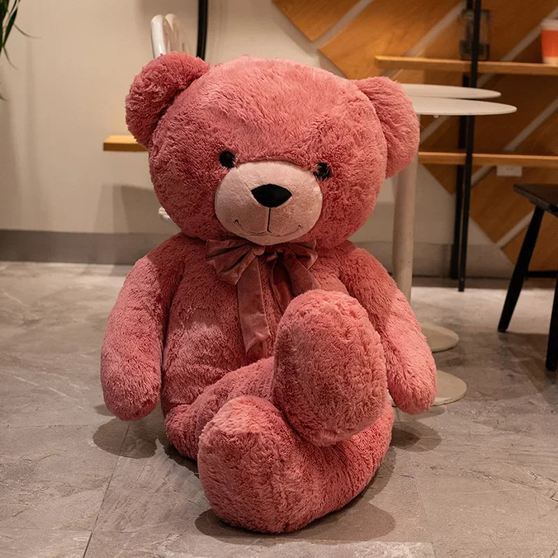 Large pink teddy bear sitting on a stone floor with a blurred indoor background