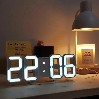 Digital clock on a table with a lamp and candle in the background