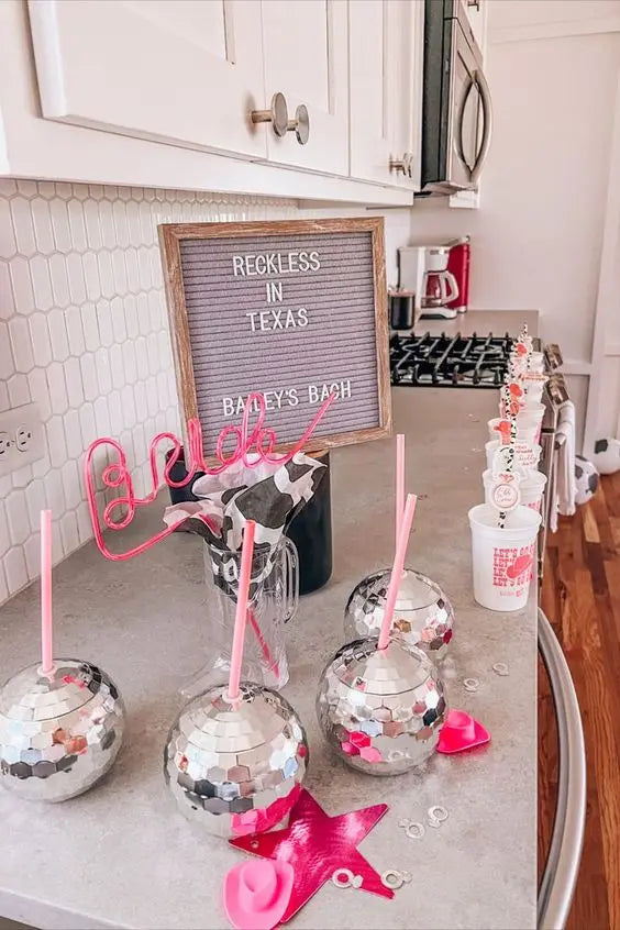 Decorative drink glasses with pink straws on a kitchen counter, featuring a 'Reckless in Texas' sign.
