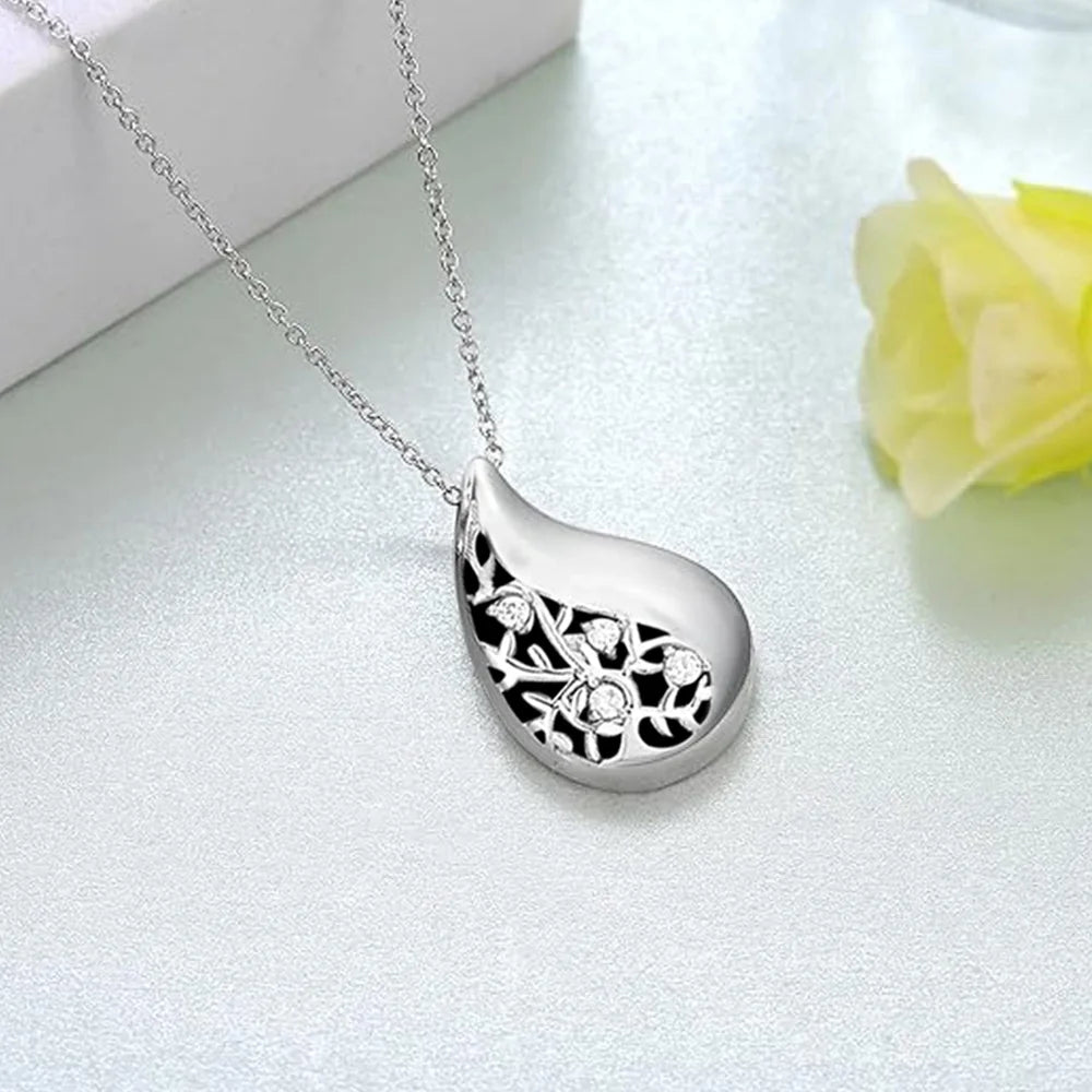 Silver teardrop-shaped pendant necklace on a light gray background with a yellow flower.