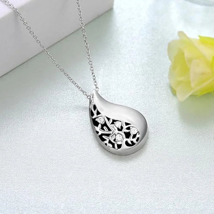 Silver teardrop-shaped pendant necklace on a light gray background with a yellow flower.