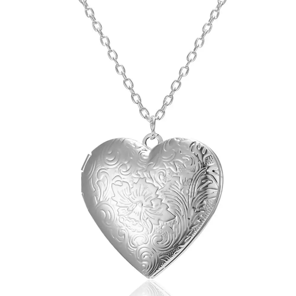 Silver heart-shaped locket with intricate designs on a white background