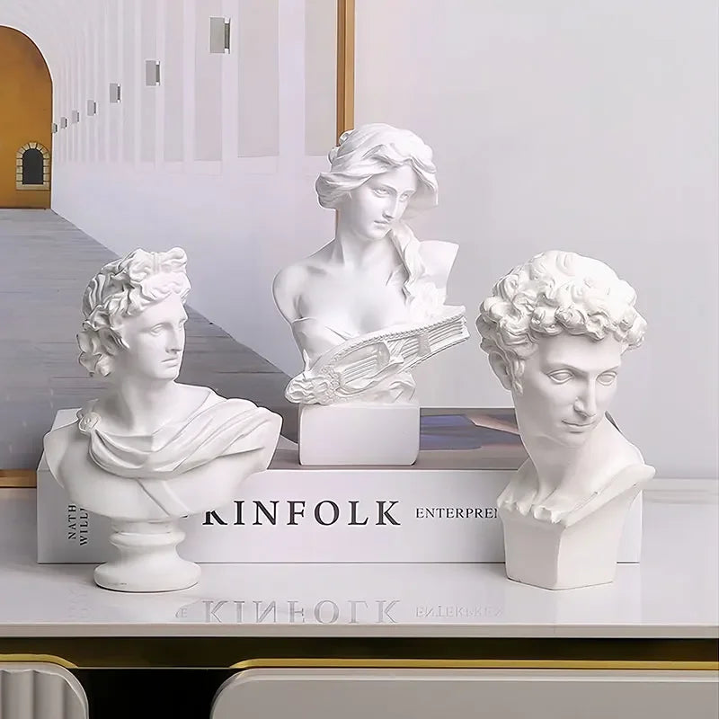 Three white classical busts on top of 'KINFOLK' books with a blurred architectural background.