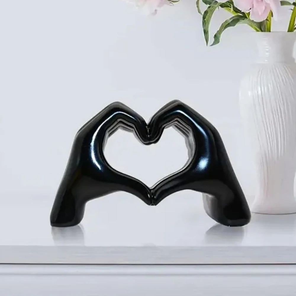 Black heart-shaped sculpture on a white surface with a vase and flowers in the background