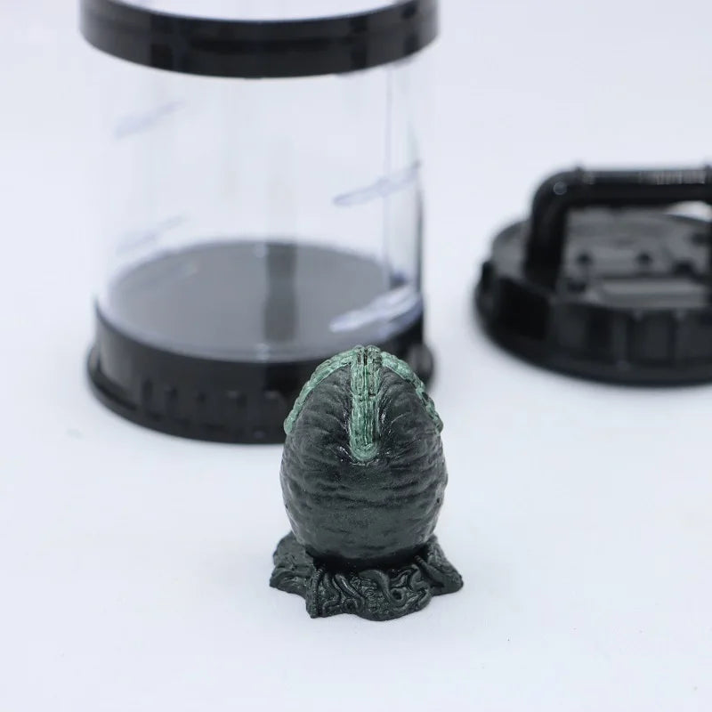 Small green figurine on a white surface with a clear container and black lid in the background.