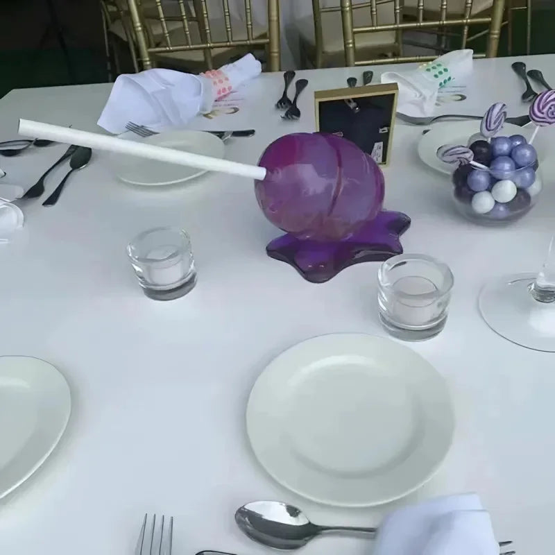 Dessert table setting with purple decorative item, plates, and glasses.