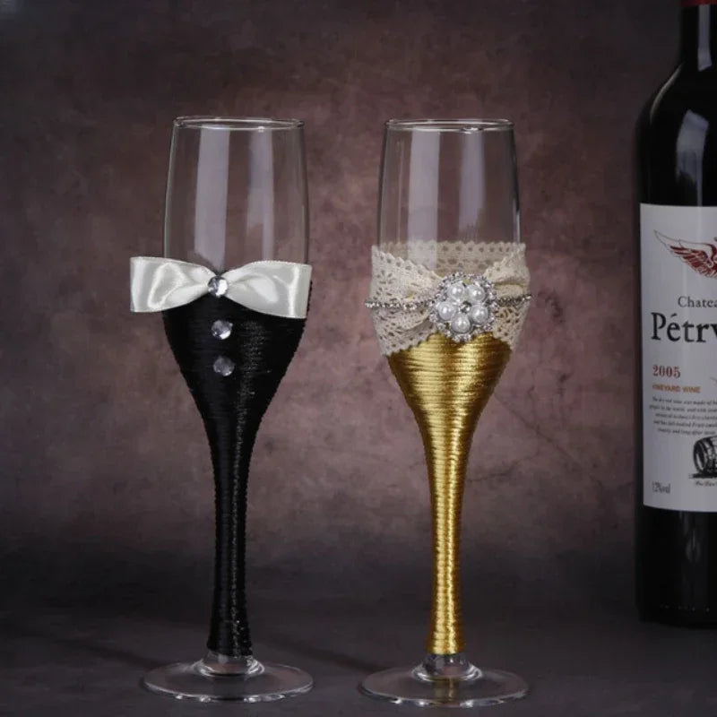 Two decorated champagne flutes with a bottle of wine in the background.