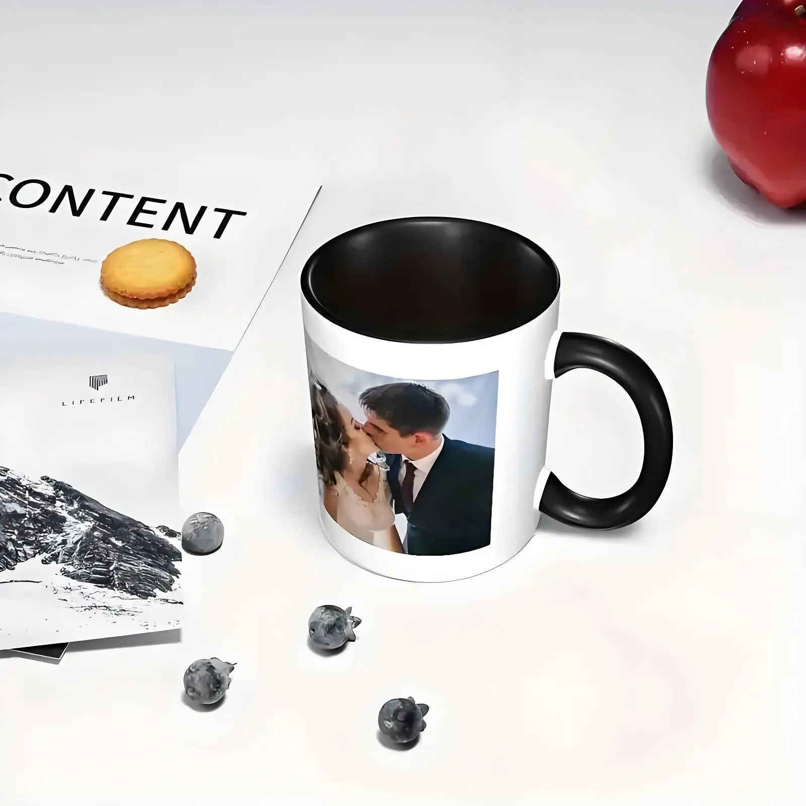 Mug with a printed photo of a couple on a white surface with an apple and magazine.