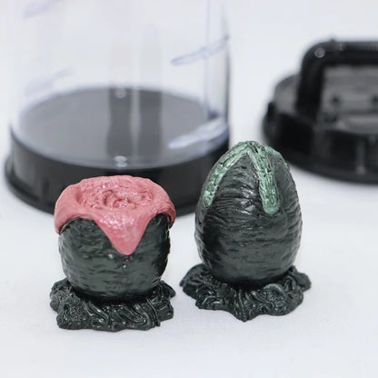 Two dinosaur egg-shaped figurines with pink and green tops on a white surface.