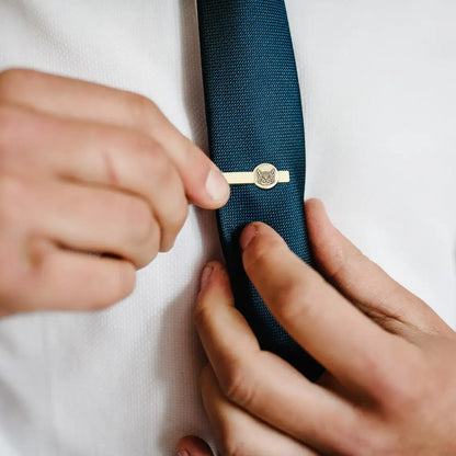 Person adjusting a gold tie clip on a blue tie against a white shirt.