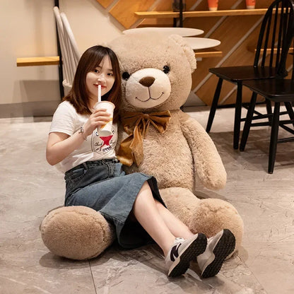 Woman sitting on the floor with a large teddy bear, holding a drink.