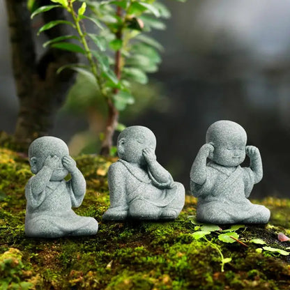 Three stone statues of a monk with a closed eye, a raised hand, and a lowered hand on a mossy surface.