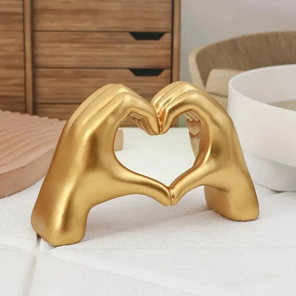 Gold decorative piece shaped like two hands forming a heart on a white surface.