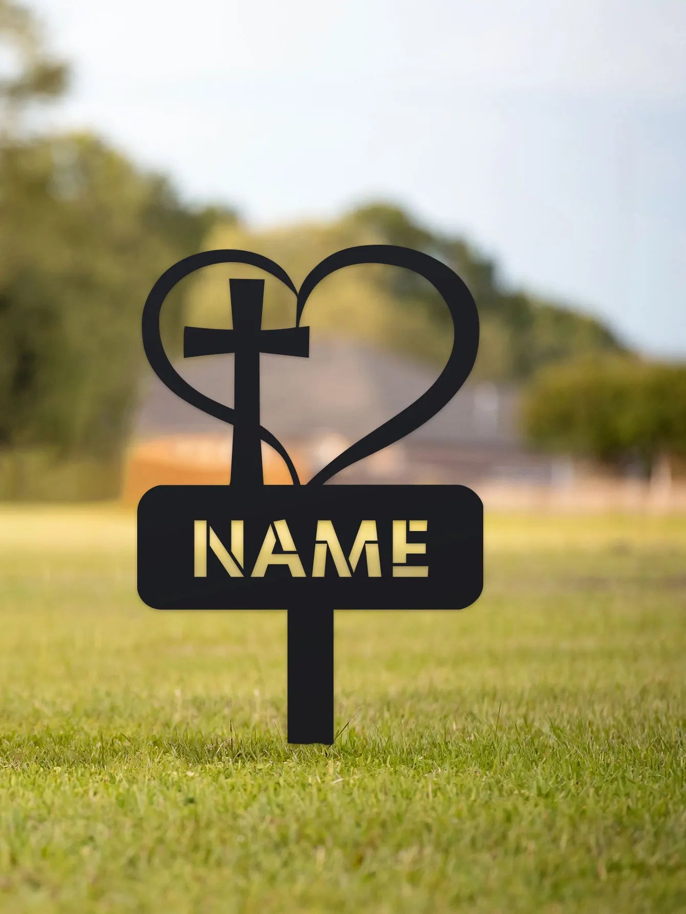Black metal sign with cross and heart design on a grassy field