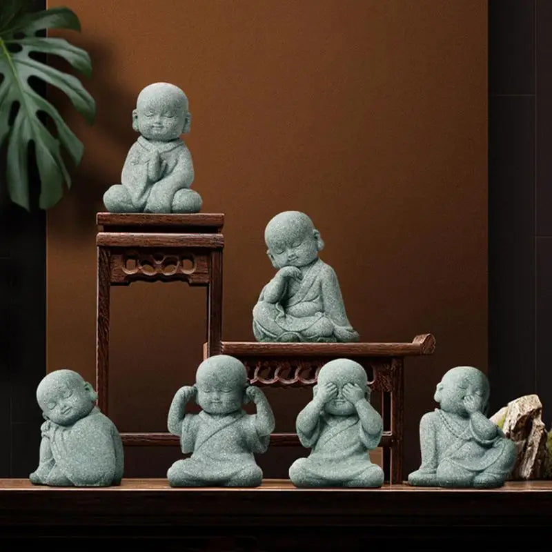 Set of six small stone statues resembling meditating children on a wooden shelf against a brown wall.