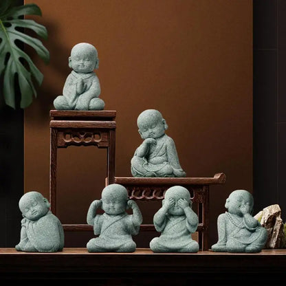 Set of six small stone statues resembling meditating children on a wooden shelf against a brown wall.