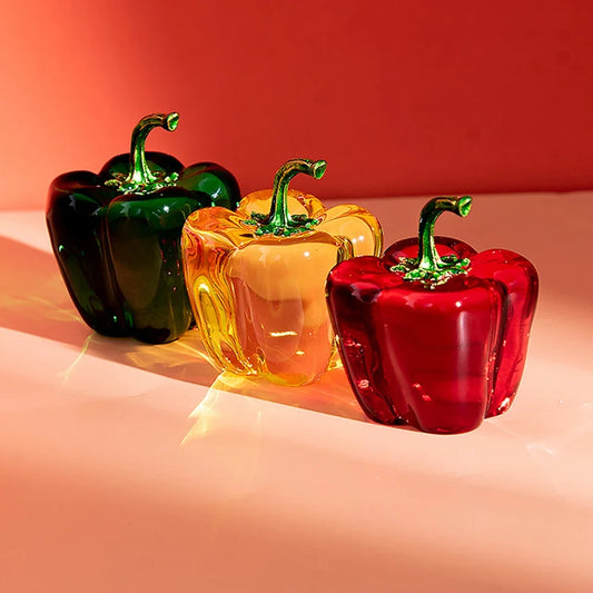 Three glass peppers in green, yellow, and red on a peach background