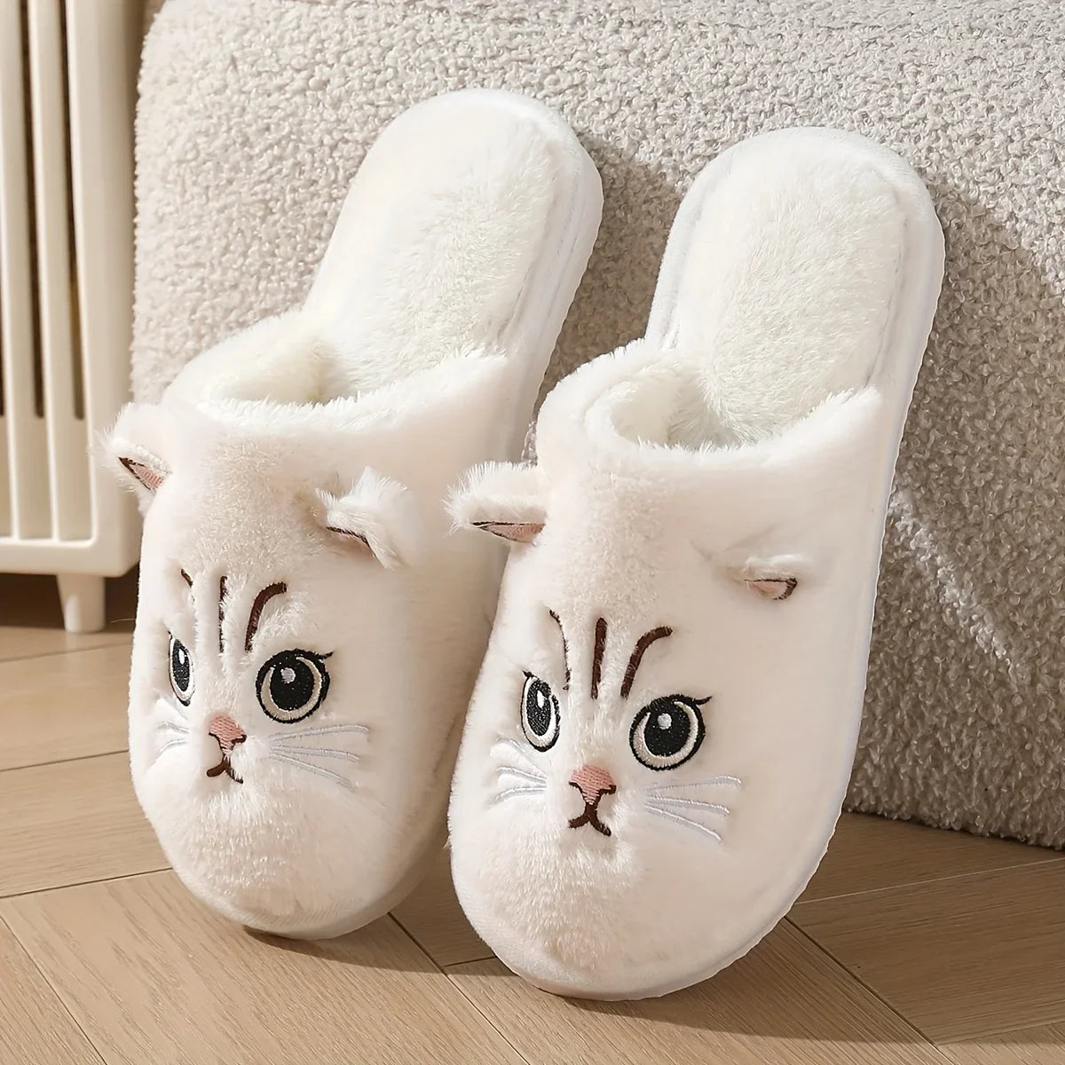 Pair of white cat-shaped slippers on a wooden floor.