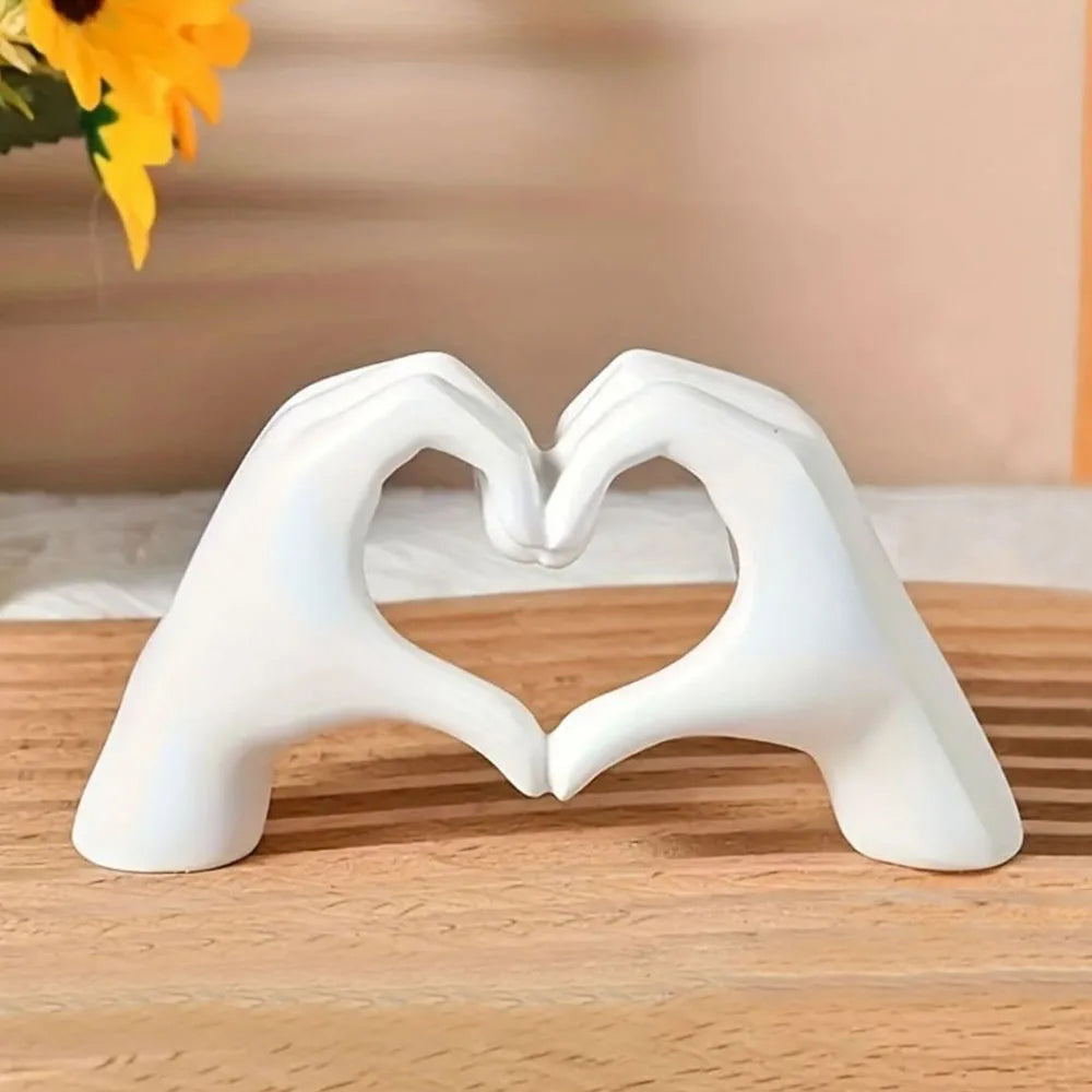 White ceramic hands forming a heart shape on a wooden surface with a blurred background