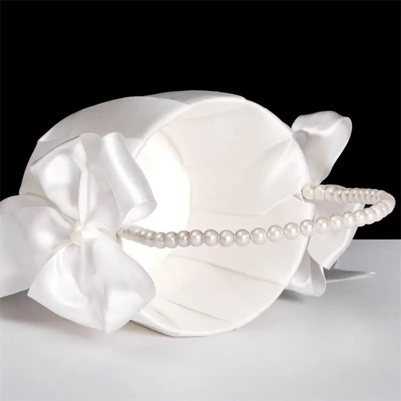 White satin headband with large bow and pearl headband on a light gray background