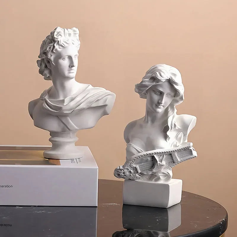 Two white classical busts on a reflective surface with a beige background