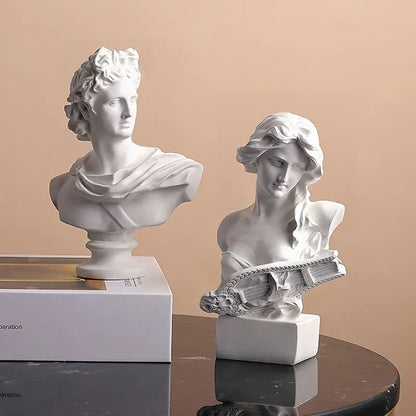 Two white classical busts on a reflective surface with a beige background