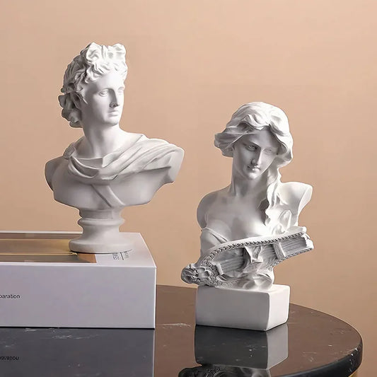 Two white classical busts on a reflective surface with a beige background