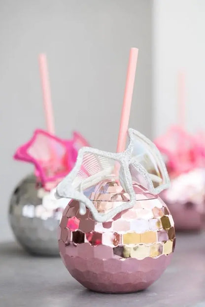 Pink disco ball-style cup with a straw and white candy on a gray background