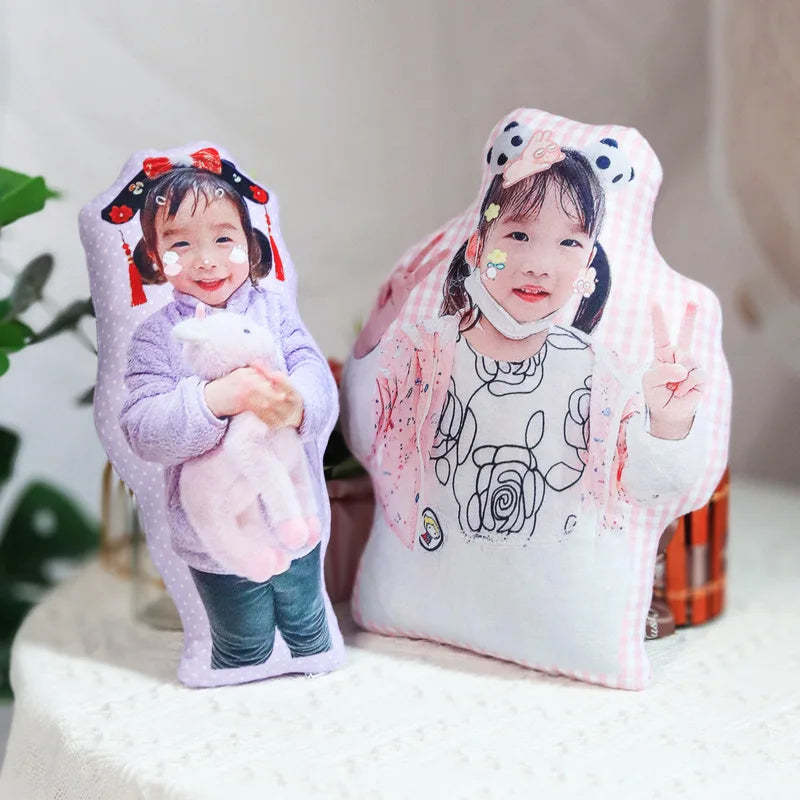 Two plush toys with printed images of children on a white surface.