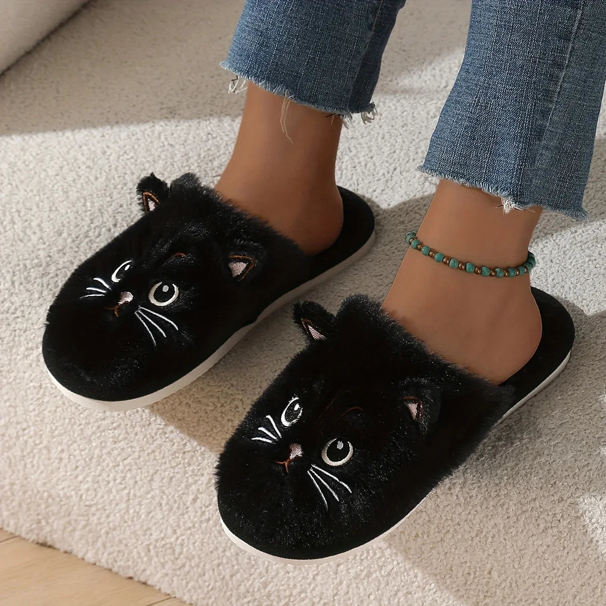 Black cat slippers worn with denim jeans on a light carpet.