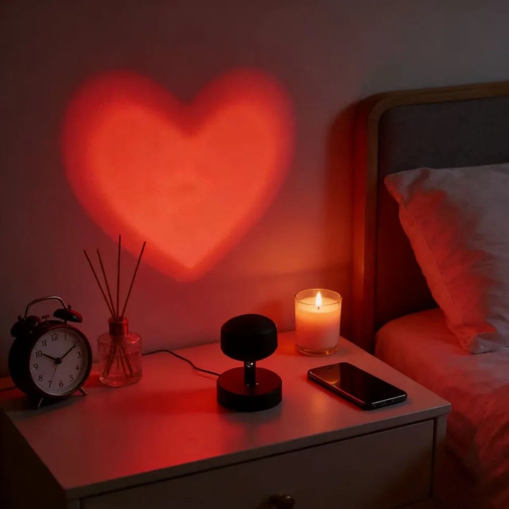 Heart-shaped light projection on a wall above a bedside table with a lit candle, phone, and clock.