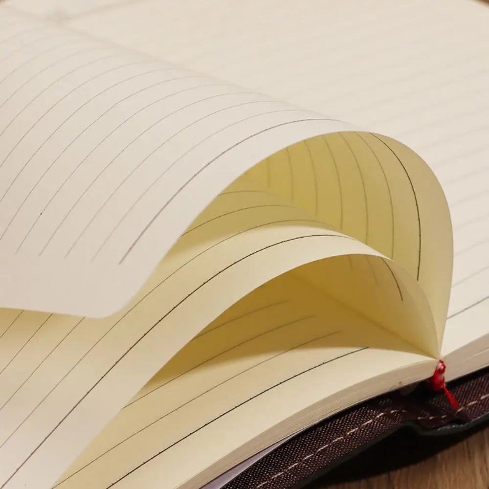 Open notebook with lined pages and a red ribbon bookmark on a wooden surface.