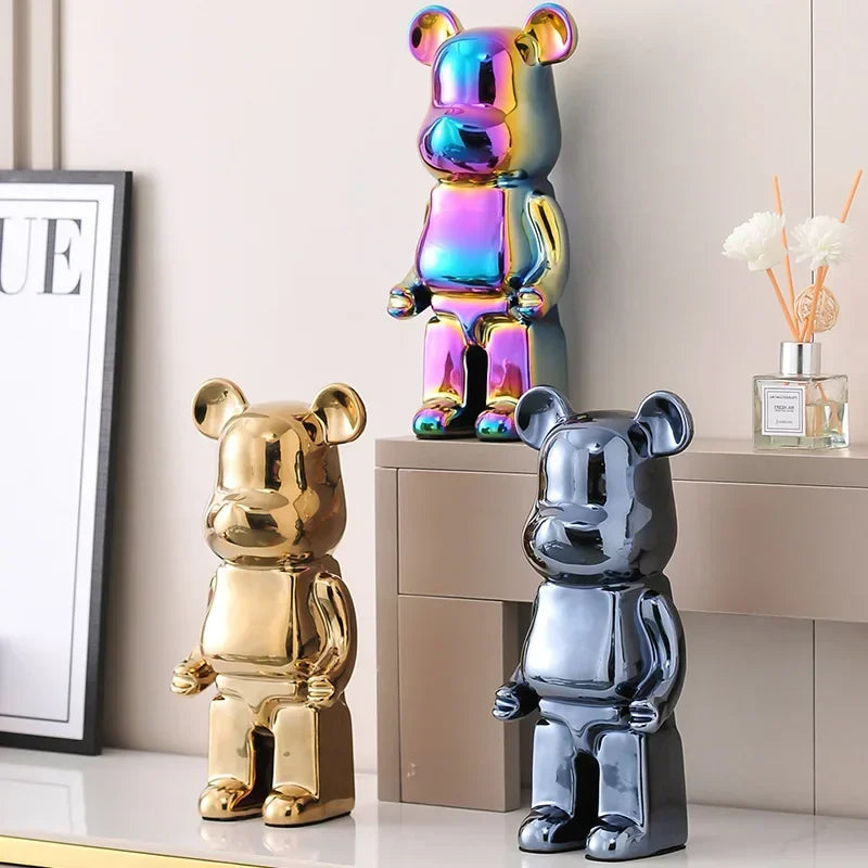 Three metallic bear figurines in gold, iridescent, and silver on a light-colored surface.