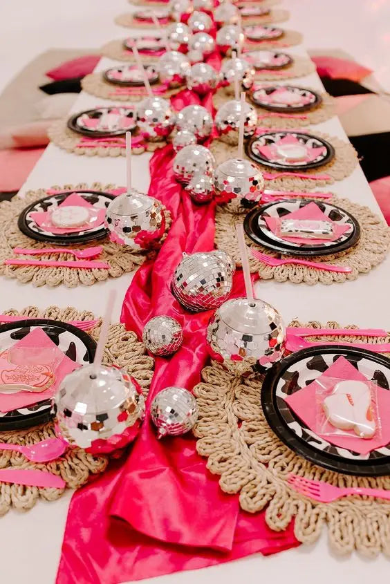 Decorative table setting with pink napkins, black plates, and silver ornaments on a white tablecloth.