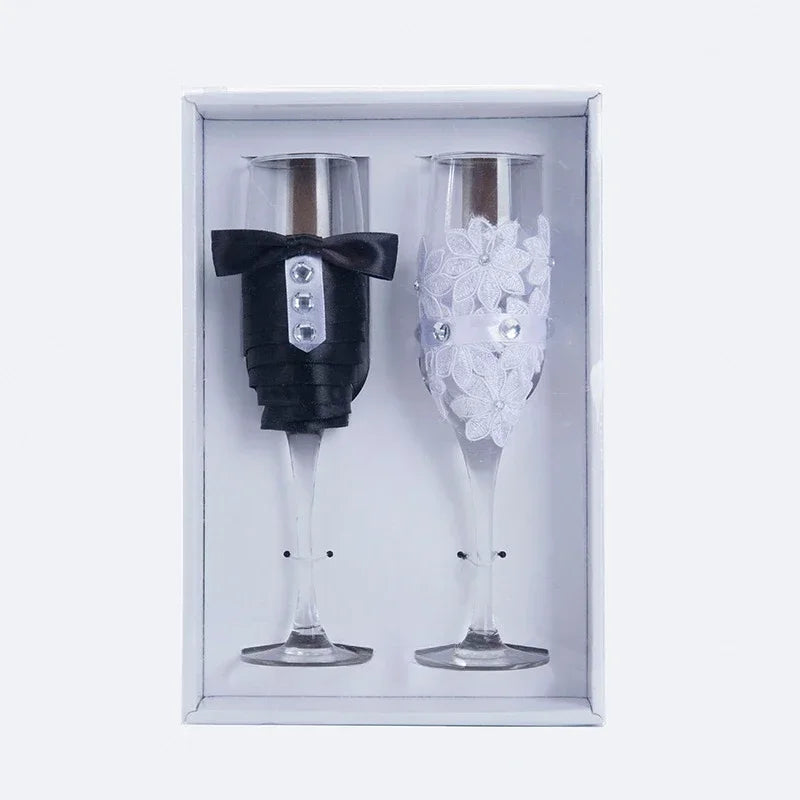 Two decorative champagne flutes, one with a tuxedo design and the other with floral design, in a box.
