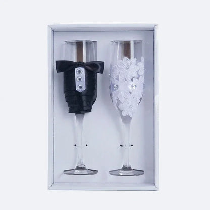 Two decorative champagne flutes, one with a tuxedo design and the other with floral design, in a box.