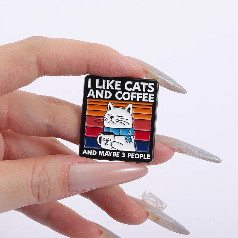 Pin with 'I Like Cats and Coffee and Maybe 3 People' text held by a hand on a white background