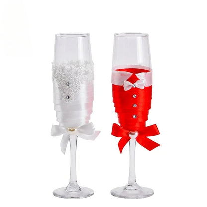 Two decorative champagne flutes, one white with a bow and embellishments, the other red with a bow and rhinestones, on a white background.