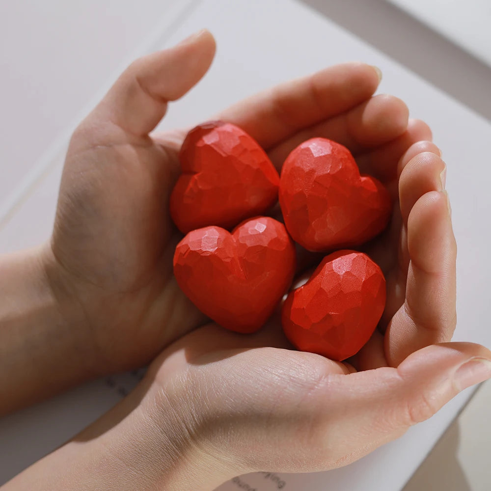 Hands holding four red heart-shaped objects against a light background
