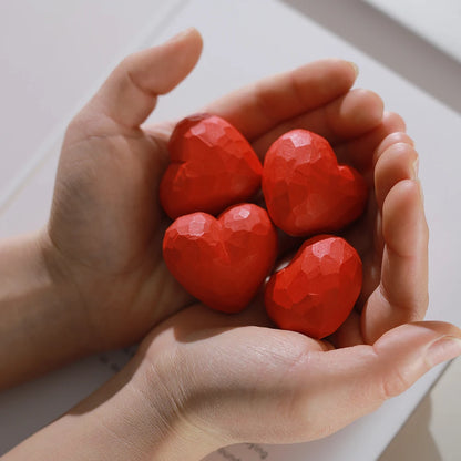 Hands holding four red heart-shaped objects against a light background