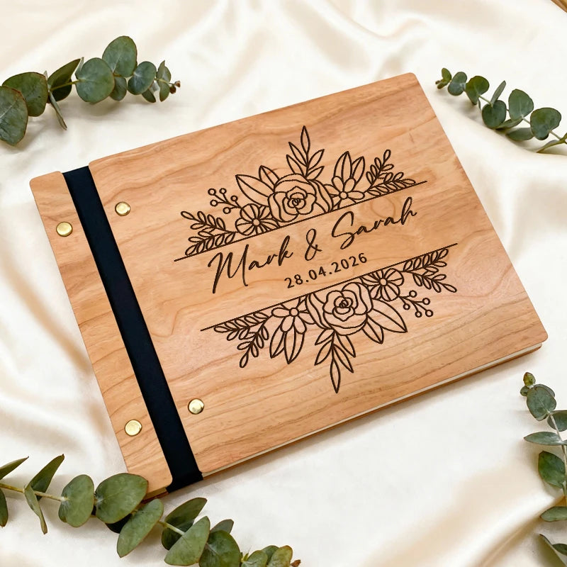 Wooden photo album with floral design and engraved text on a white background with eucalyptus leaves.