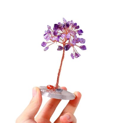 Hand holding a small crystal tree with purple stones on a white background
