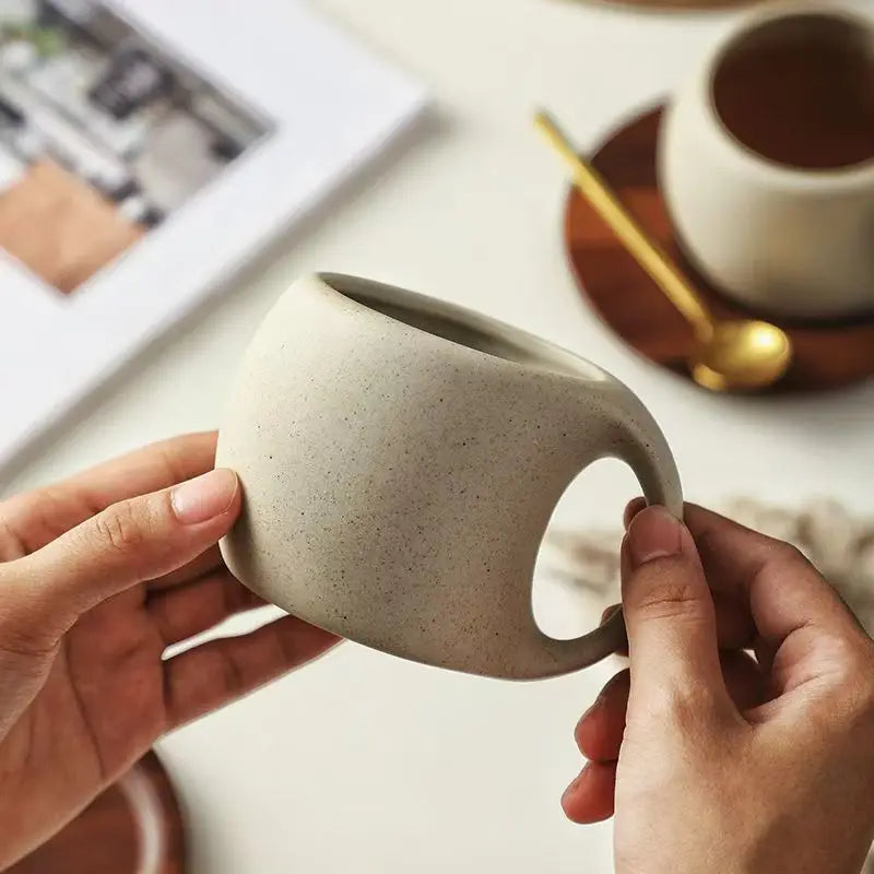 Person holding a ceramic mug with a blurred background of a table setting.