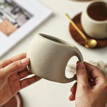 Person holding a ceramic mug with a blurred background of a table setting.