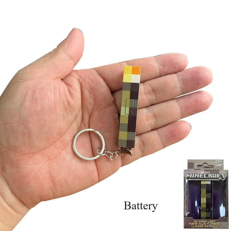 Hand holding a Minecraft-themed keychain with a battery pack, showing the product's size.